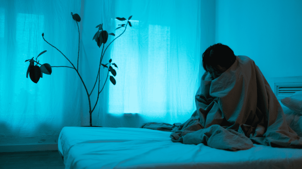 A person sitting on top of a bed in front of a window.