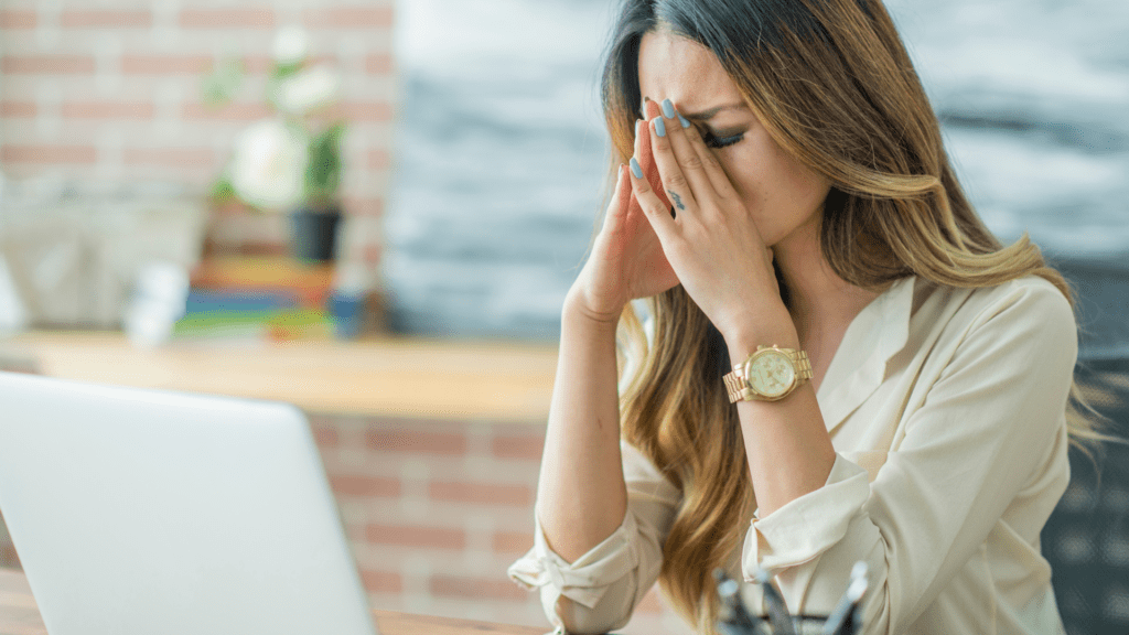 A woman sitting at a table with her hands over her face.