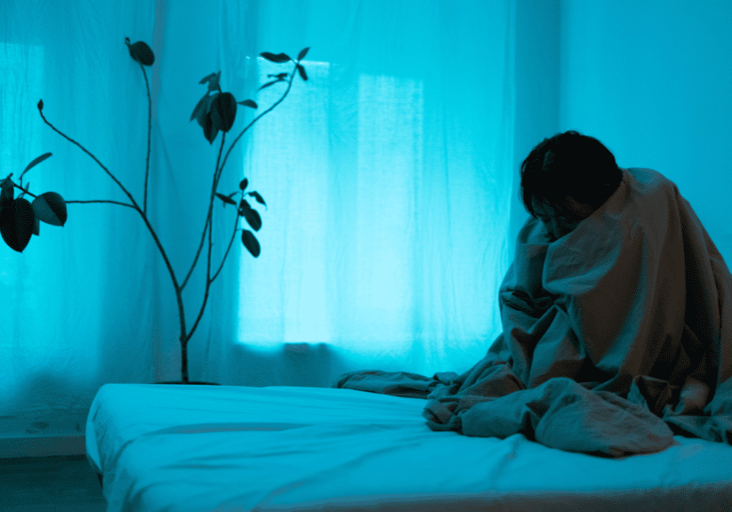 A person sitting on top of a bed in front of a window.