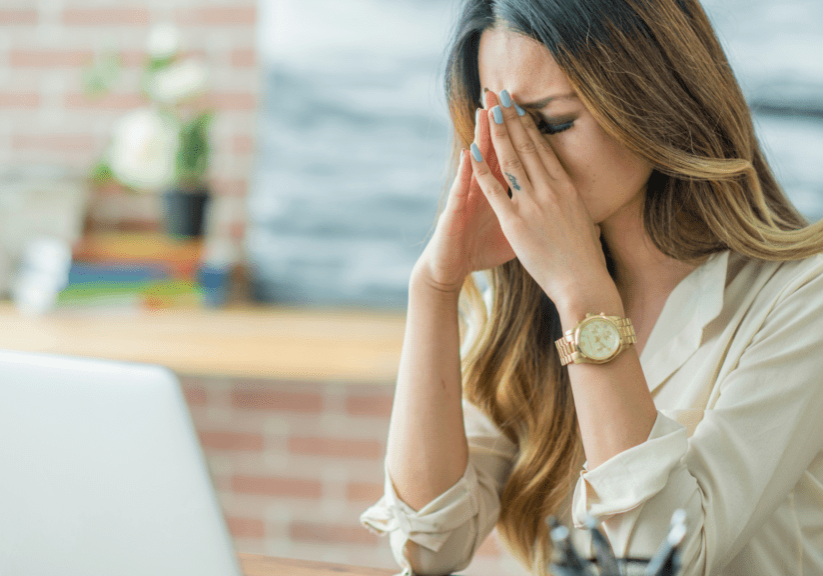 A woman sitting at a table with her hands over her face.